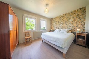 Ein Schlafzimmer mit einem Bett, zwei Fenstern, einer Heizung, einem Holzschrank und einem Nachttisch mit Lampe.