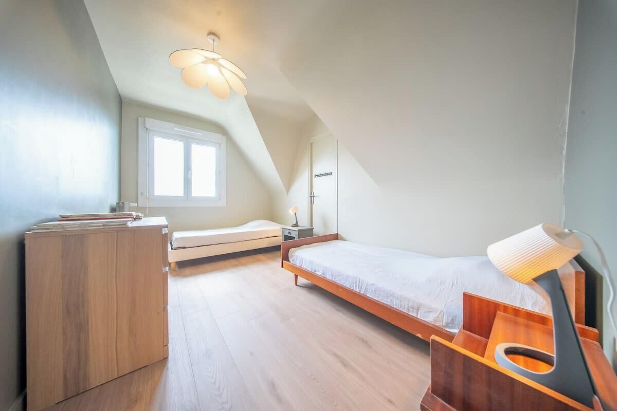 A bedroom with a sloped ceiling, a bed, a desk, and a window.