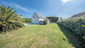 Ein eingeschossiges Haus mit geneigtem Dach, einer kleinen Veranda und einem gepflegten Rasen.