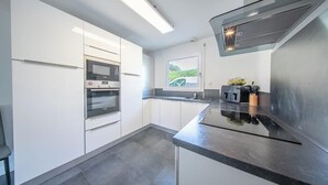 Eine moderne Küche mit weißen Schränken, einem eingebauten Backofen, einer Mikrowelle und einem Fenster mit Blick auf Grünfläche.