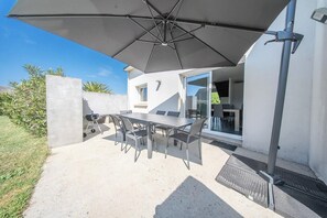 Eine Terrassengruppe im Freien mit Tisch, Stühlen, einem großen Sonnenschirm und einem Grill.