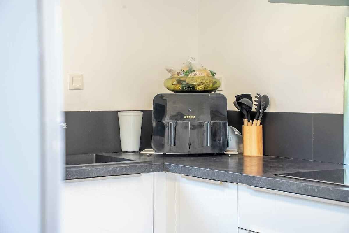 Ett kök med en svart kaffemaskin, en skål med frukt och ett förvaringsställ för köksredskap på bänkskivan.