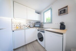 Eine kleine Küche mit weißen Schränken, einer Waschmaschine, einer Mikrowelle und einer Kaffeemaschine.