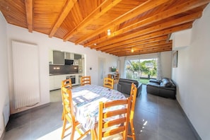 Eine moderne Küche mit weißen Schränken, ein Essbereich mit Holztisch und -stühlen sowie eine gemütliche Sitzecke mit einer Couch.