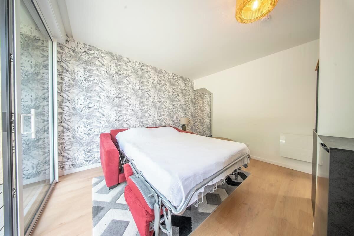 A room with a bed, a red chair, a small table, a lamp, and a patterned wallpaper.