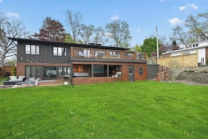Ein modernes, zweistöckiges Haus mit einer großen Veranda, einem Essbereich und einer sichtbaren Garage.