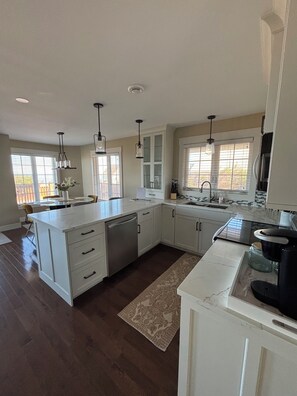 A modern kitchen with white cabinetry, a central island, pendant lighting, and a view to the outside.