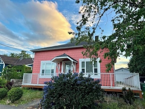 A two-story house with a red exterior, white trim, and a porch with a railing.