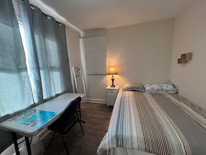 Ein Hotelzimmer mit einem Bett, einem Schreibtisch, einem Stuhl, einer Lampe, einem Spiegel und einem Fenster mit Vorhängen.