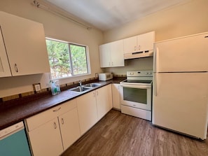 A kitchen with white cabinets, a double sink, a microwave, an oven, and a refrigerator.