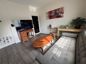 Ein Wohnzimmer mit einer Couch, einem Holztisch, einem Fernseher, einem Ventilator und einem Bild an der Wand.
