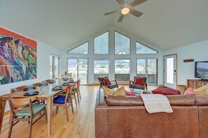 A spacious living area with a high ceiling, large windows, a dining table set, and a leather sofa.