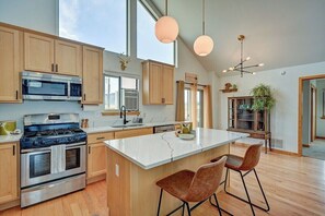 A modern kitchen with wooden cabinets, stainless steel appliances, a large island with bar stools, and pendant lighting.