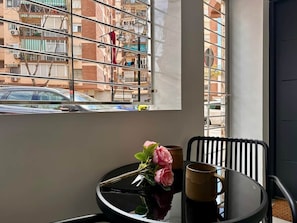 Ein Zimmer mit Fensterblick auf eine Stadtlandschaft, einem runden Tisch mit Blumenvase und einem Stuhl.