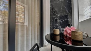 Ein Zimmer mit Glastür, Marmorwand, rundem Tisch mit Tassen und Blumen sowie einem Stuhl.