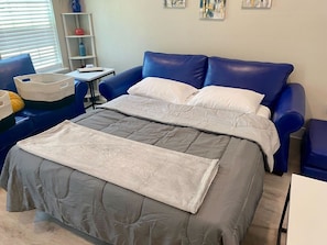 Un dormitorio con una cama, un sofá azul, una mesita y una estantería con adornos.
