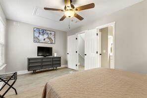 A bedroom with a bed, a TV on a dresser, a ceiling fan, and a painting on the wall.