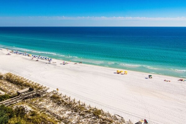 A beach with a wooden walkway, clear blue water, and a sandy shore.