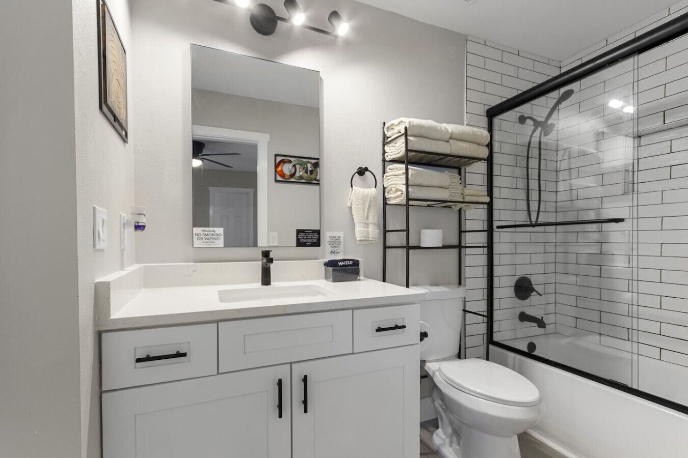 Une salle de bain moderne avec un lavabo blanc, un miroir et des toilettes. On y trouve un espace douche avec des portes en verre et un porte-serviettes avec des serviettes pliées.