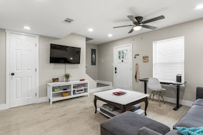 A living room with a TV, a ceiling fan, a white sofa, a coffee table, and a desk with a chair.