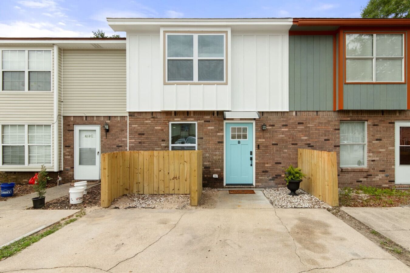 Une rangée de maisons de ville avec une porte bleue au centre, une façade en briques et des clôtures en bois.