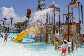 A water park with a large yellow slide, a wooden play structure, and a clear blue sky.