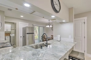 A kitchen with a marble countertop, stainless steel appliances, and pendant lighting.