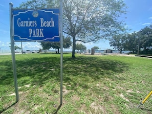 A sign for Garniers Beach Park with a grassy area and trees in the background.