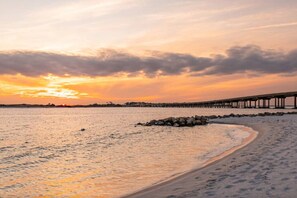 A beach with a pier extending into the water, a clear sky, and a sunset.