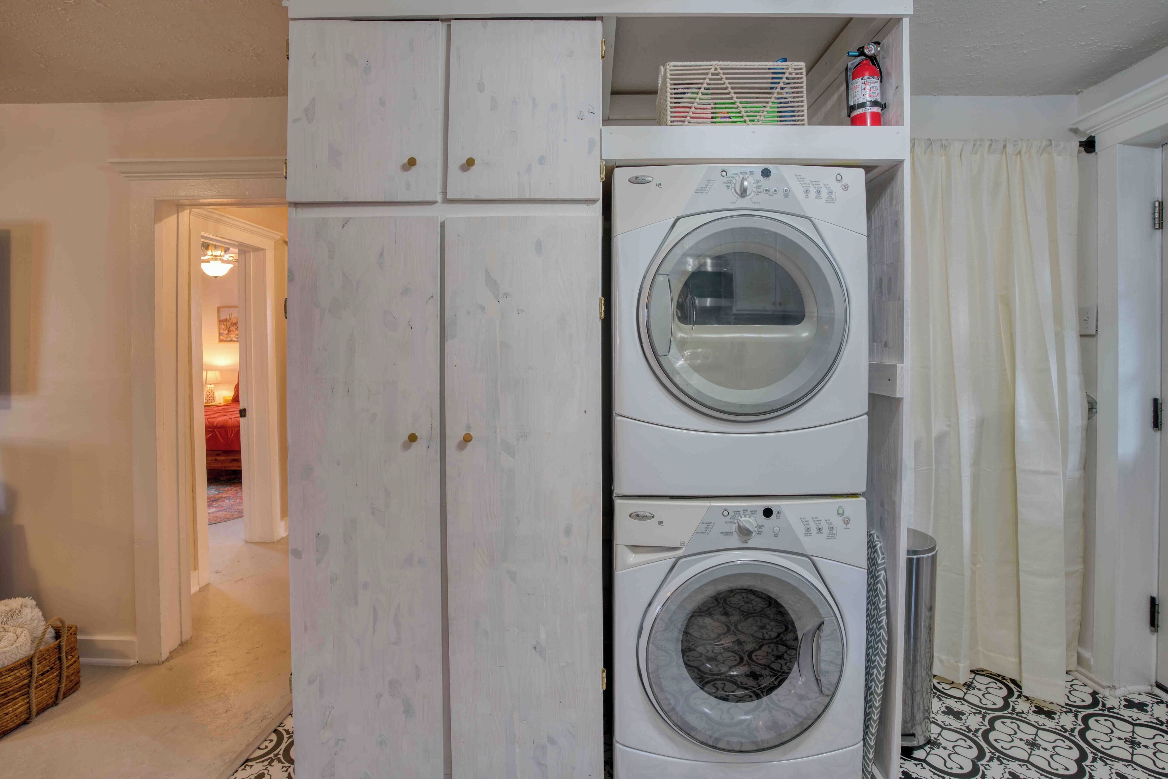 A laundry room with two stacked washing machines, a fire extinguisher, and a trash can.