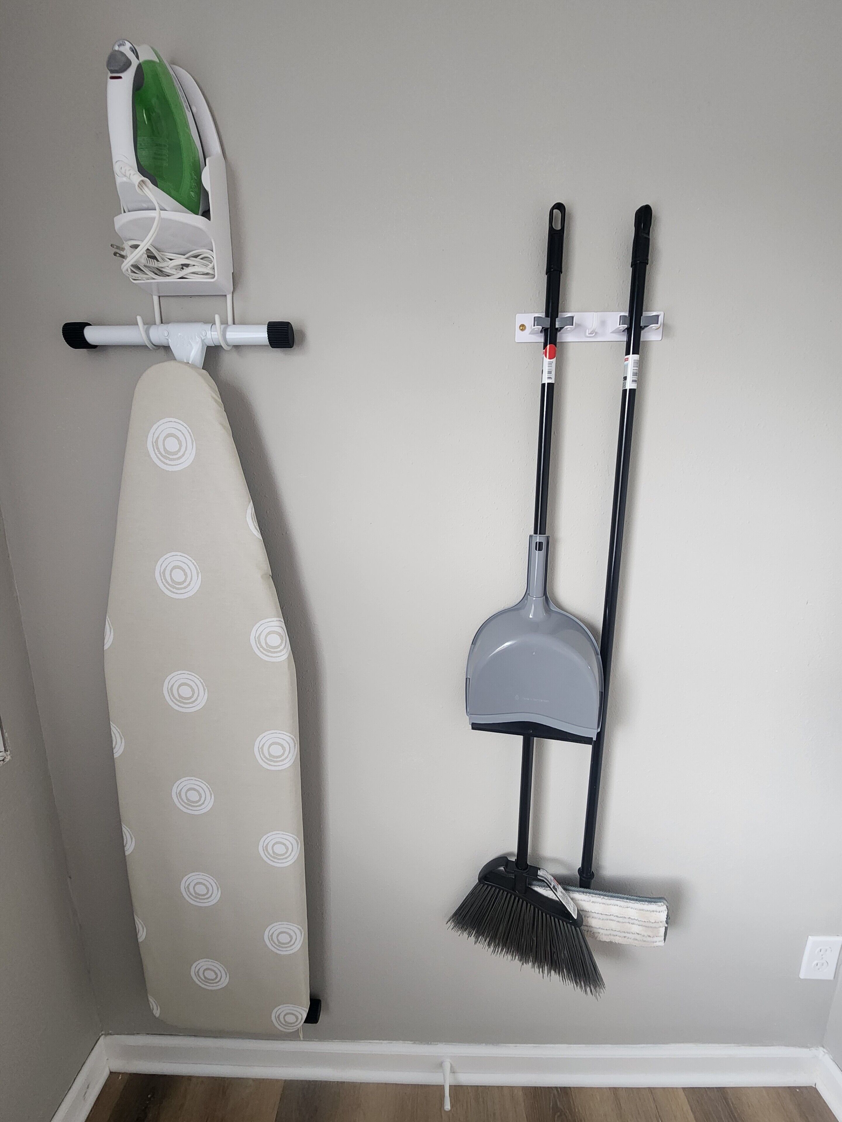 A wall-mounted ironing board with an iron and a broom.