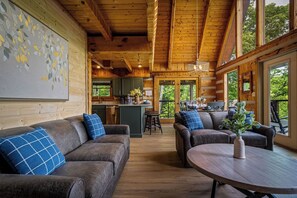 Ein Holzblockhaus-Interieur mit einer Küche, zwei Sofas, einem runden Tisch und großen Fenstern.