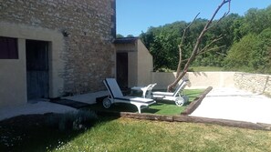 Ein Steinhaus mit einer kleinen Terrasse, ausgestattet mit zwei weißen Liegestühlen und einem Tisch.