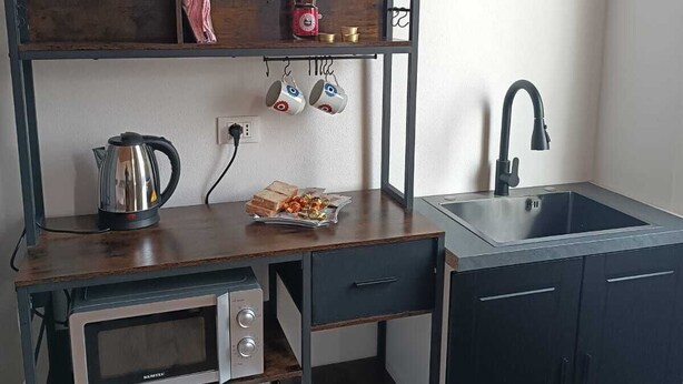 Una kitchenette compacta con microondas, refrigerador, lavamanos y estantes de madera con utensilios de cocina.
