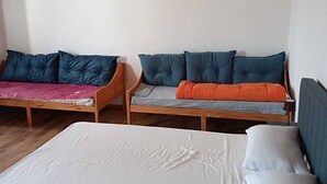 Una habitación con una cama grande, dos camas más pequeñas con ropa de cama de colores diferentes y un techo de madera.