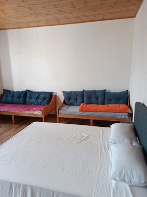 Ein Zimmer mit einem großen Bett, zwei kleineren Betten mit unterschiedlicher Bettwäsche und einer Holzbalkendecke.