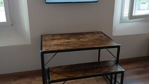 Habitación con piso de madera, una mesa con estructura metálica y un televisor en la pared mostrando a un esquiador.