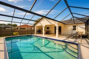 A swimming pool with a clear blue water feature, a covered patio area with outdoor furniture, and a house in the background. - Modern Port Charlotte Retreat with Heated Pool (Port Charlotte)