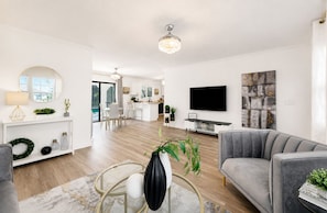 En moderne stue med en grå sofa, et fjernsyn og et spiseområde med hvide møbler.