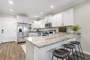 Una cocina moderna con armarios blancos, una isla grande con taburetes, un refrigerador y un microondas.