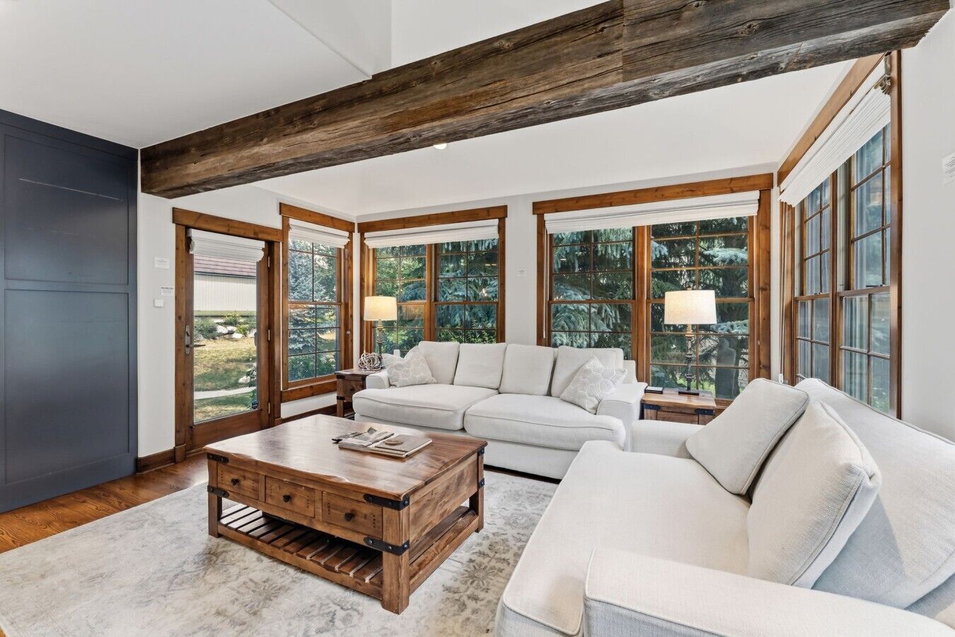 A spacious living room with a large window, a white sofa, a wooden coffee table, and a dark accent wall.