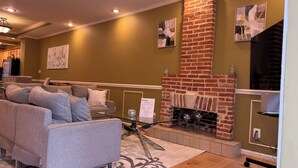 A living room with a brick fireplace, a sofa, and a glass coffee table. - Free Parking, Walking Distance, Camden Yards, M&T Stadium, U of MD, Convention (Baltimore)
