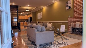 A living room with a sofa, a glass coffee table, a fireplace, and a kitchen in the background. - Free Parking, Walking Distance, Camden Yards, M&T Stadium, U of MD, Convention (Baltimore)