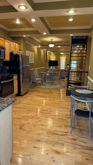 A spacious kitchen with modern appliances, a dining area with a round table and chairs, and a staircase leading to an upper level.