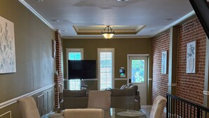 A dining area with a round table, four chairs, a chandelier, a television, and a brick wall. - Free Parking, Walking Distance, Camden Yards, M&T Stadium, U of MD, Convention (Baltimore)