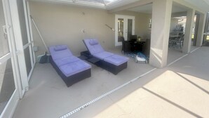 Un espacio exterior cubierto con dos sillones, una mesa y una puerta que da a un ambiente interior.