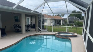 Una piscina con hidromasaje, un porche cubierto con sillas y vistas a casas vecinas.