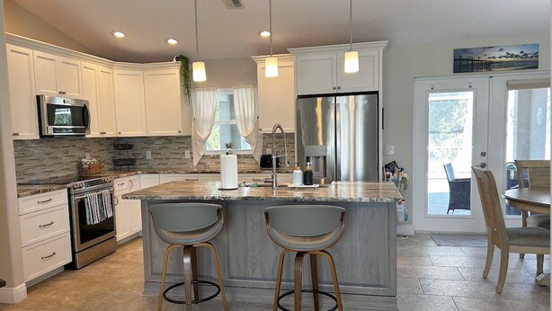 Una cocina moderna con armarios blancos, un refrigerador de acero inoxidable, una isla grande con taburetes de bar y un comedor con mesa y sillas.
