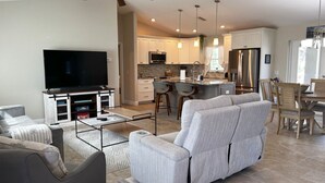 Una sala de estar moderna con sofá, televisor y comedor con sillas y una mesa.
