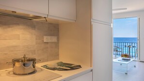 Une cuisine moderne avec une casserole sur le plan de travail, une fenêtre donnant sur la mer et un balcon agrémenté de mobilier d’extérieur.